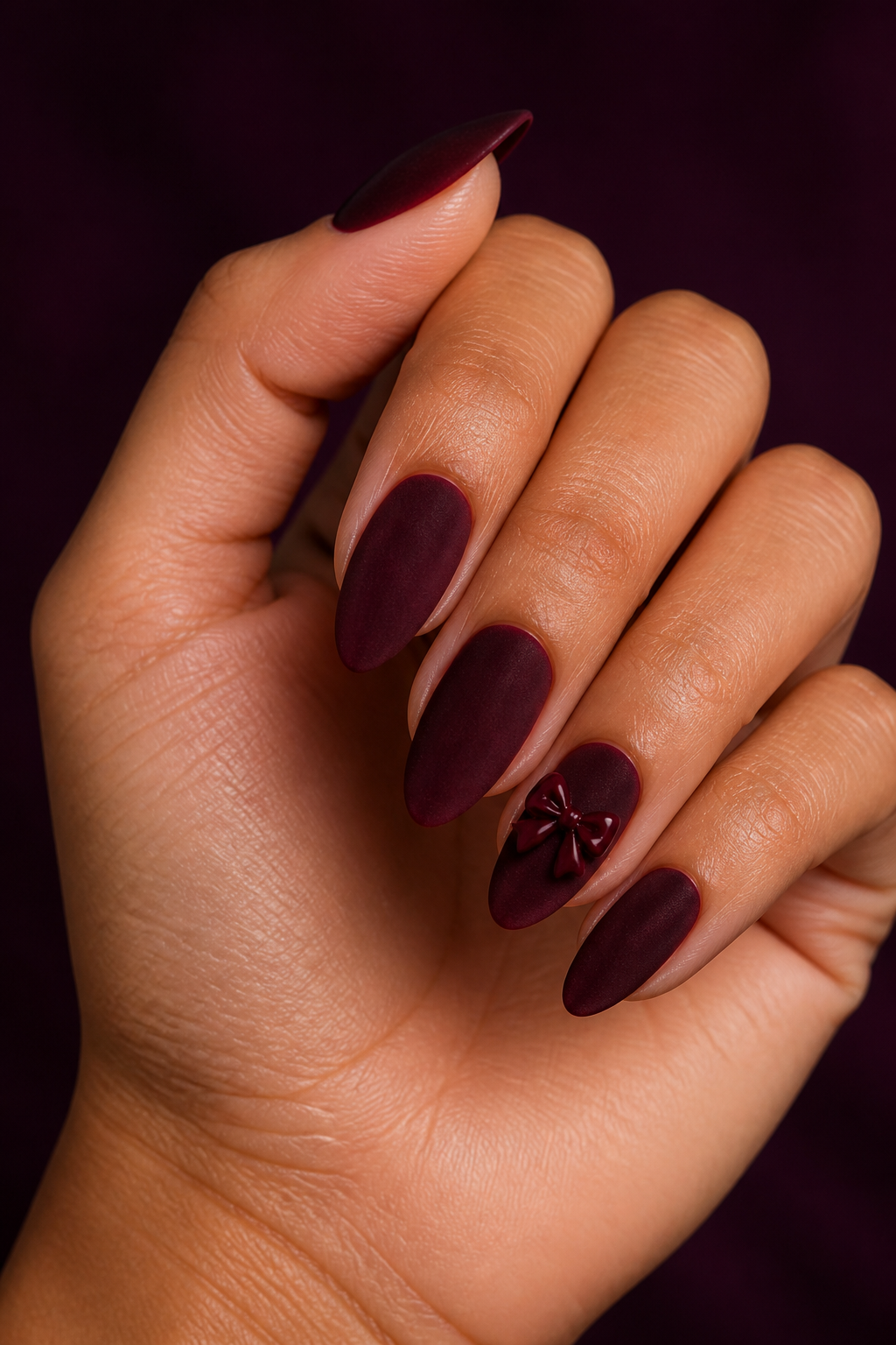 Velvet burgundy Christmas nails with a glossy bow accent.