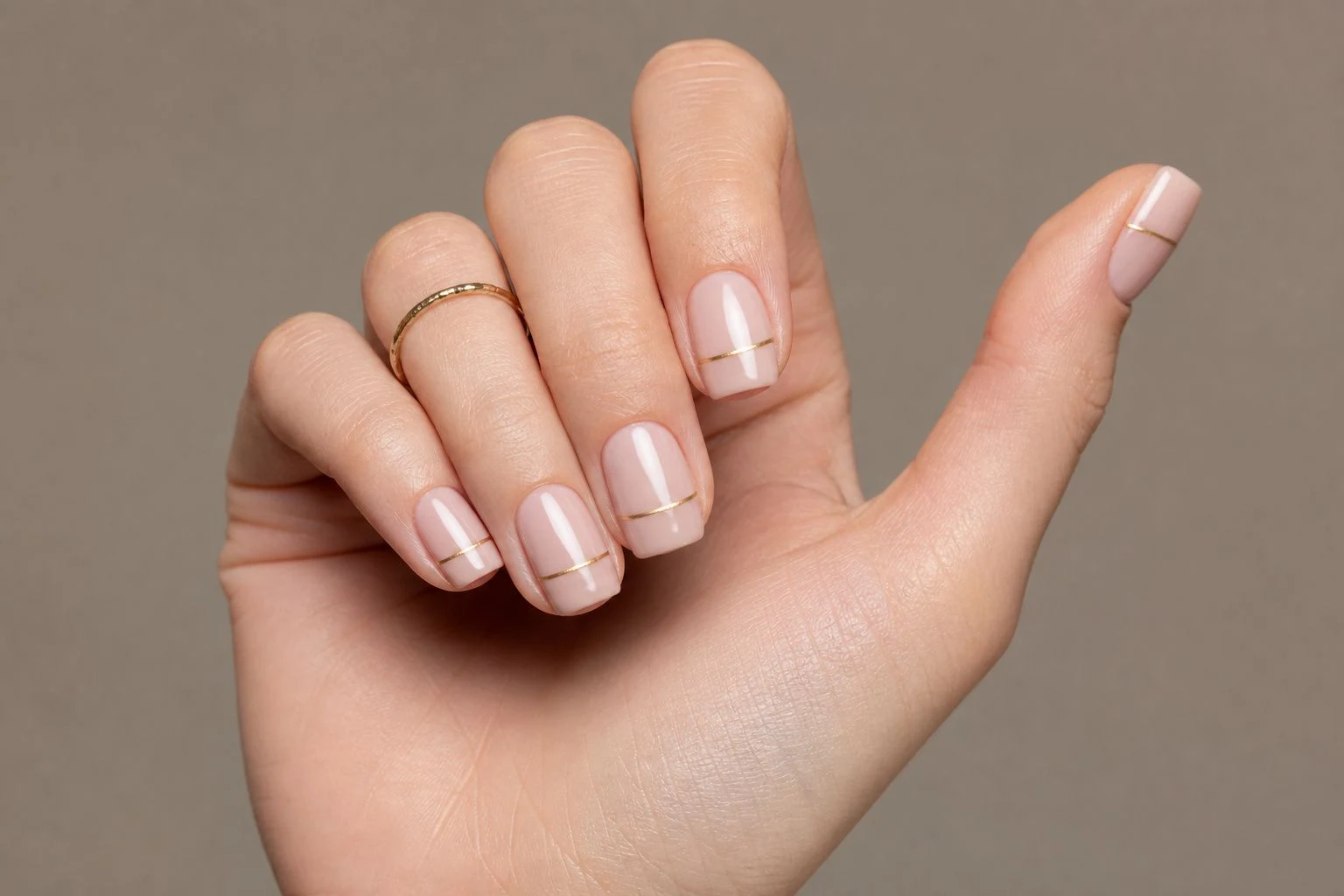 Short nude square Christmas nails with a fine gold line in a curled hand pose with a delicate gold ring