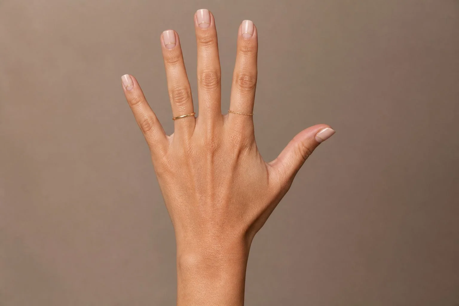 Short nude square Christmas nails with a fine gold line accent and two thin gold rings, open palm pose