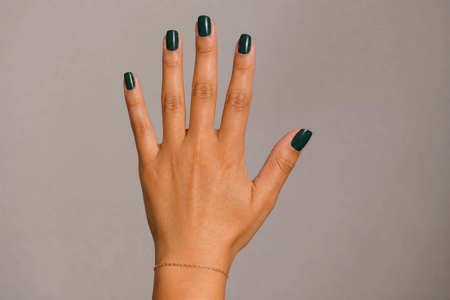 Deep evergreen green square Christmas nails with a delicate gold bracelet, open palm pose