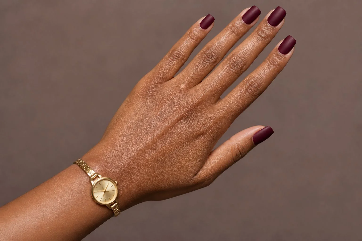 Matte burgundy square Christmas nails with a slim gold watch, diagonal hand pose