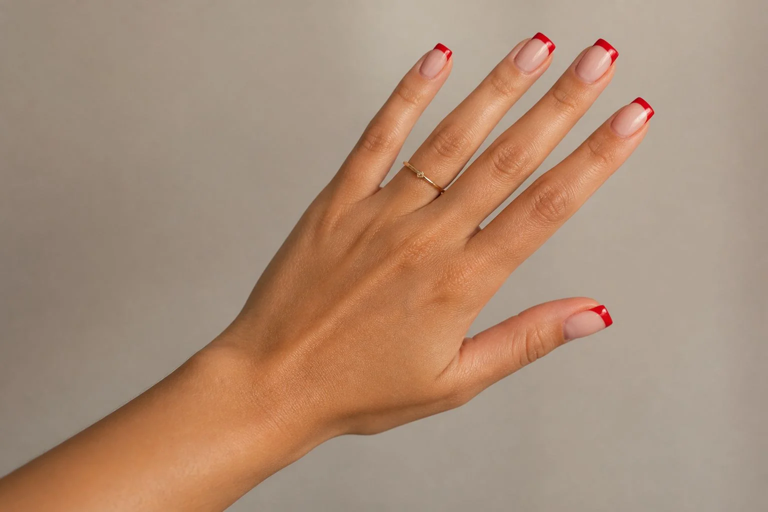 Red square French Christmas nails with a delicate gold ring, reaching hand pose