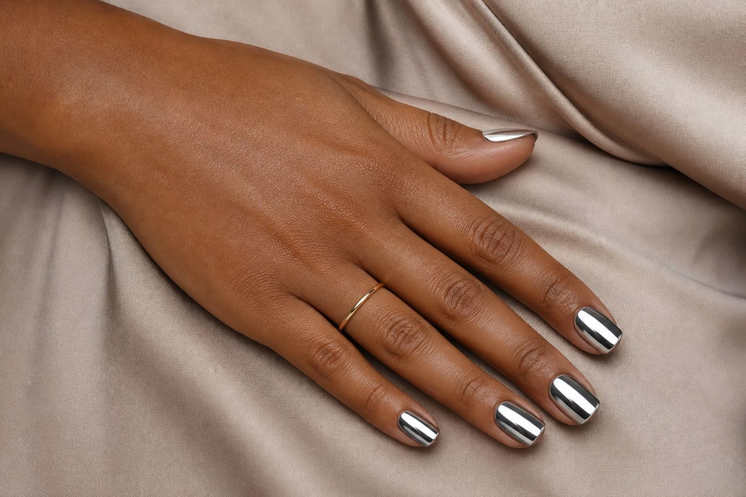 Silver chrome square Christmas nails resting at the hip with a delicate gold ring