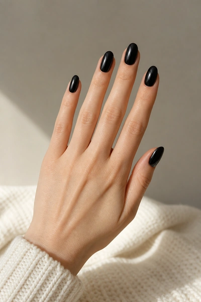 Glossy black oval nails on a fair skin tone hand in a relaxed diagonal fan pose with visible wrist and short partial forearm, natural daylight
