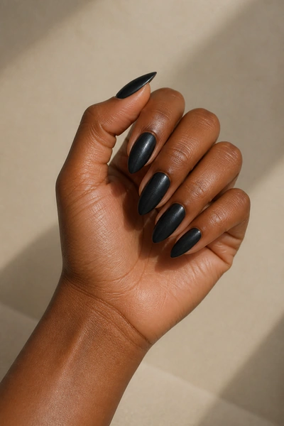 Near-black almond nails on a deep brown skin tone hand in a fingertip-rest pose with visible wrist and short partial forearm, natural daylight