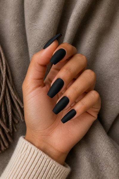 Velvet matte black coffin nails on a tan skin tone hand in a gentle pinch pose with visible wrist and short partial forearm, natural daylight