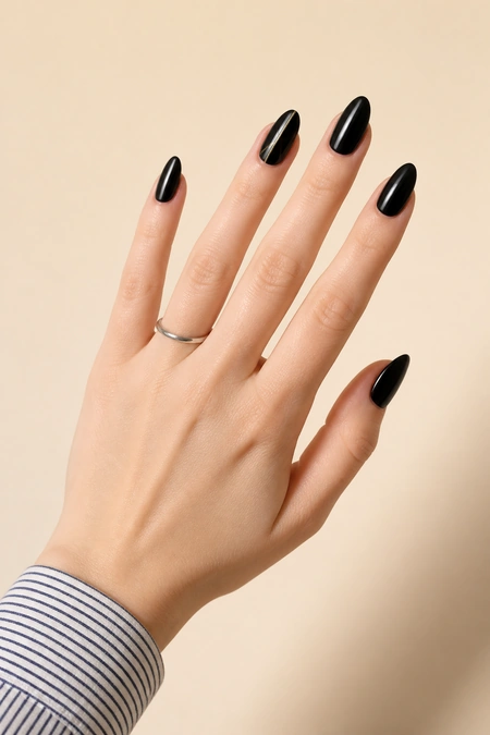 Black nails with a fine gold accent on a fair skin tone hand in an open diagonal display with visible wrist and short partial forearm, natural daylight