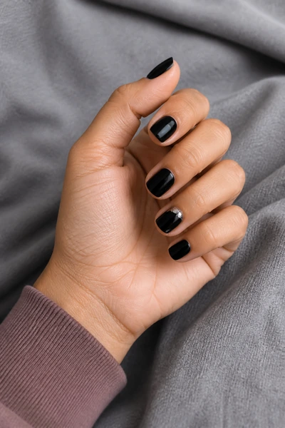 Short black nails with one silver accent on a light brown skin tone hand in a gentle pinch pose with visible wrist and short partial forearm, natural daylight
