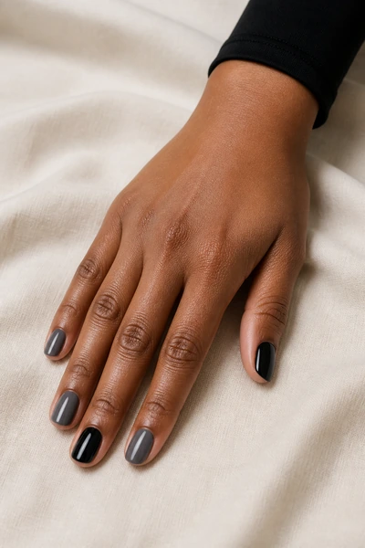 Short black and smoky grey alternating nails on a medium deep skin tone hand in a palm-down three-quarter pose with visible wrist and short partial forearm, natural daylight