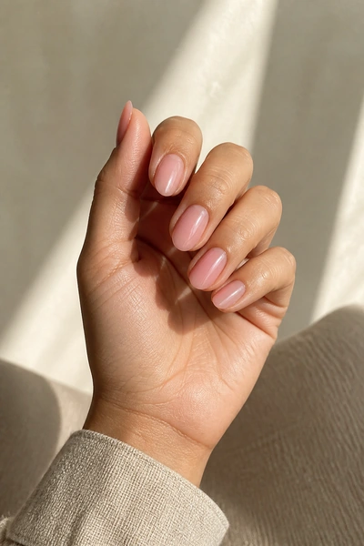 Sheer blush duck nails on a medium skin tone hand in a softly curled pose with visible wrist and short partial forearm, natural daylight