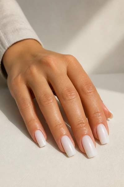Milky white duck nails on a tan skin tone hand in a fingertip-rest pose with visible wrist and short partial forearm, natural daylight