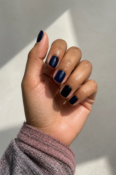 Short glossy navy duck nails on a light brown skin tone hand in a softly curled pose with visible wrist and short partial forearm, natural daylight