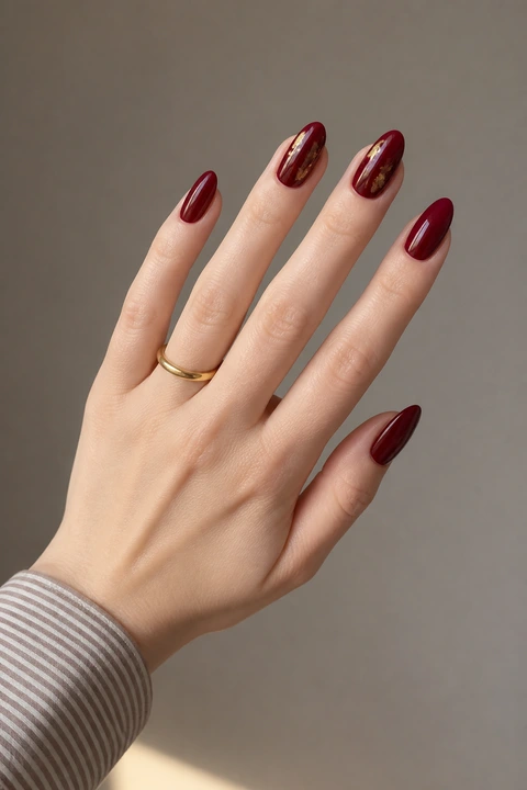 dark cherry red glossy nails with irregular gold flecks on a light skin tone hand with visible wrist