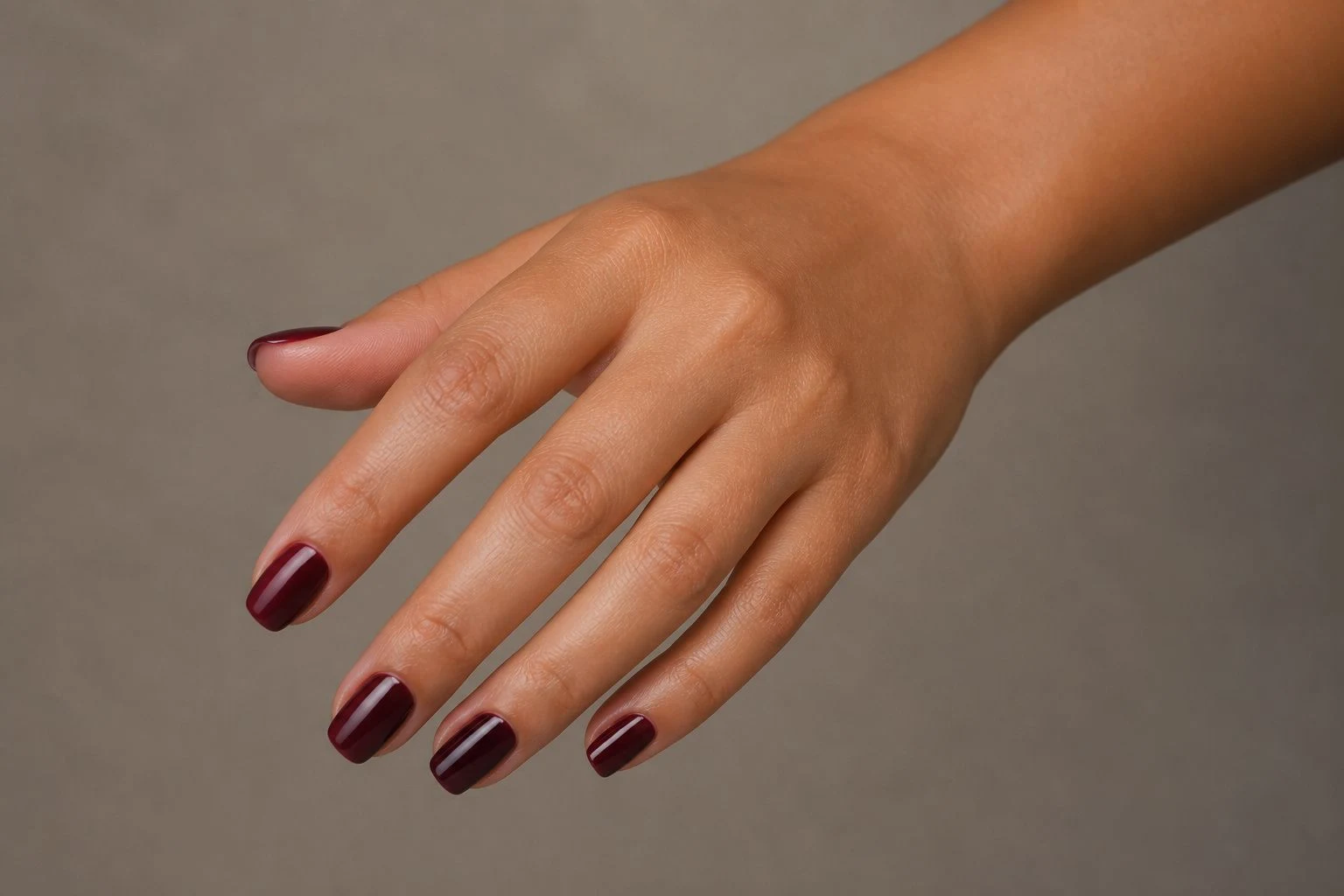 Short square burgundy nails in a curled hand pose with nail tops facing the camera