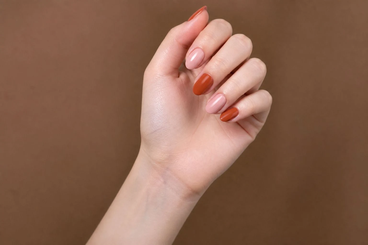 Blush and rust accent nails in a curled hand pose with wrist turned outward