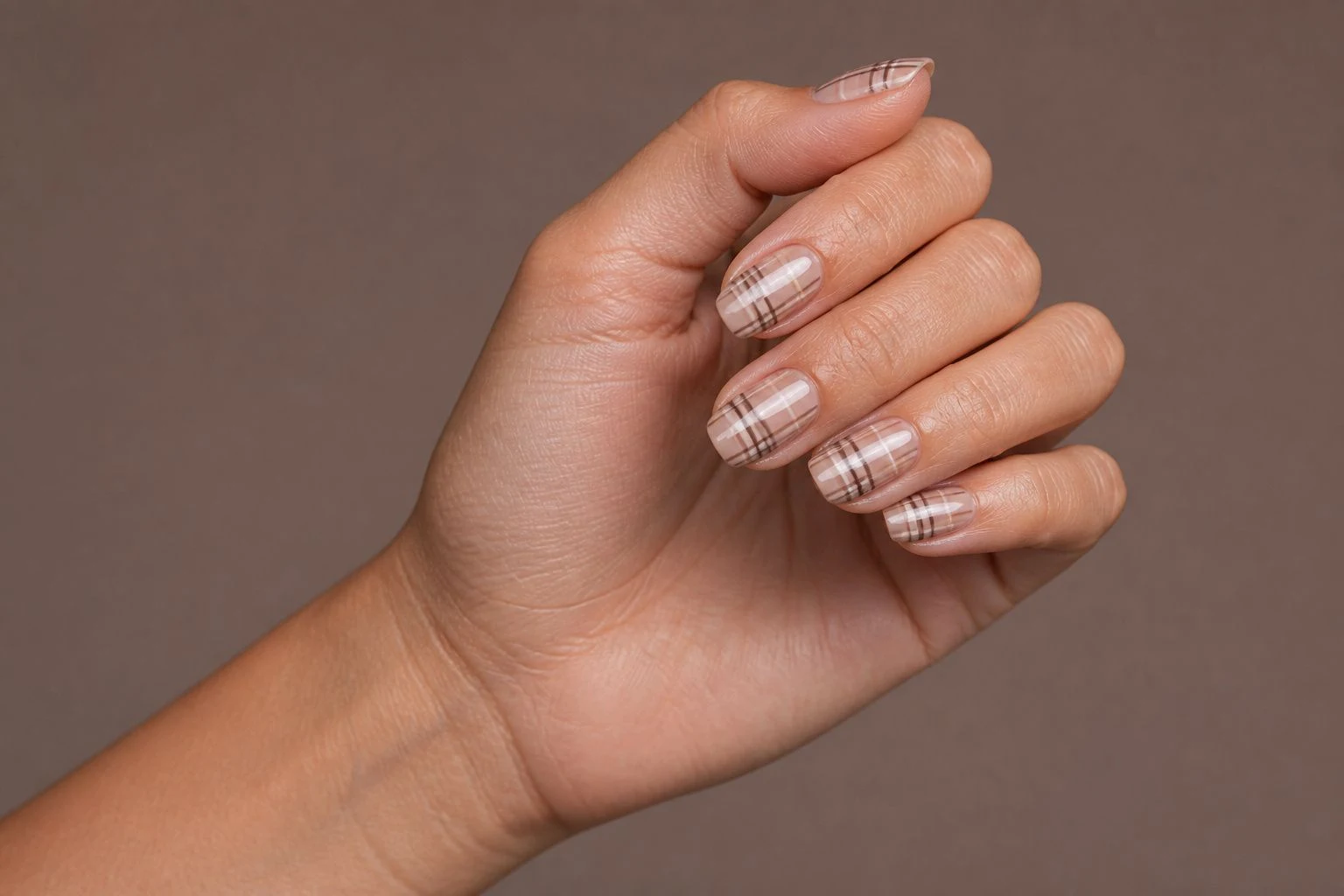 Brown plaid pattern nails in a curled hand pose showing all five fingers
