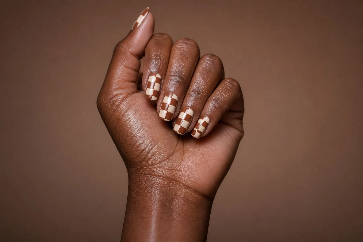 Chocolate checkered pattern nails in an elevated curled hand pose