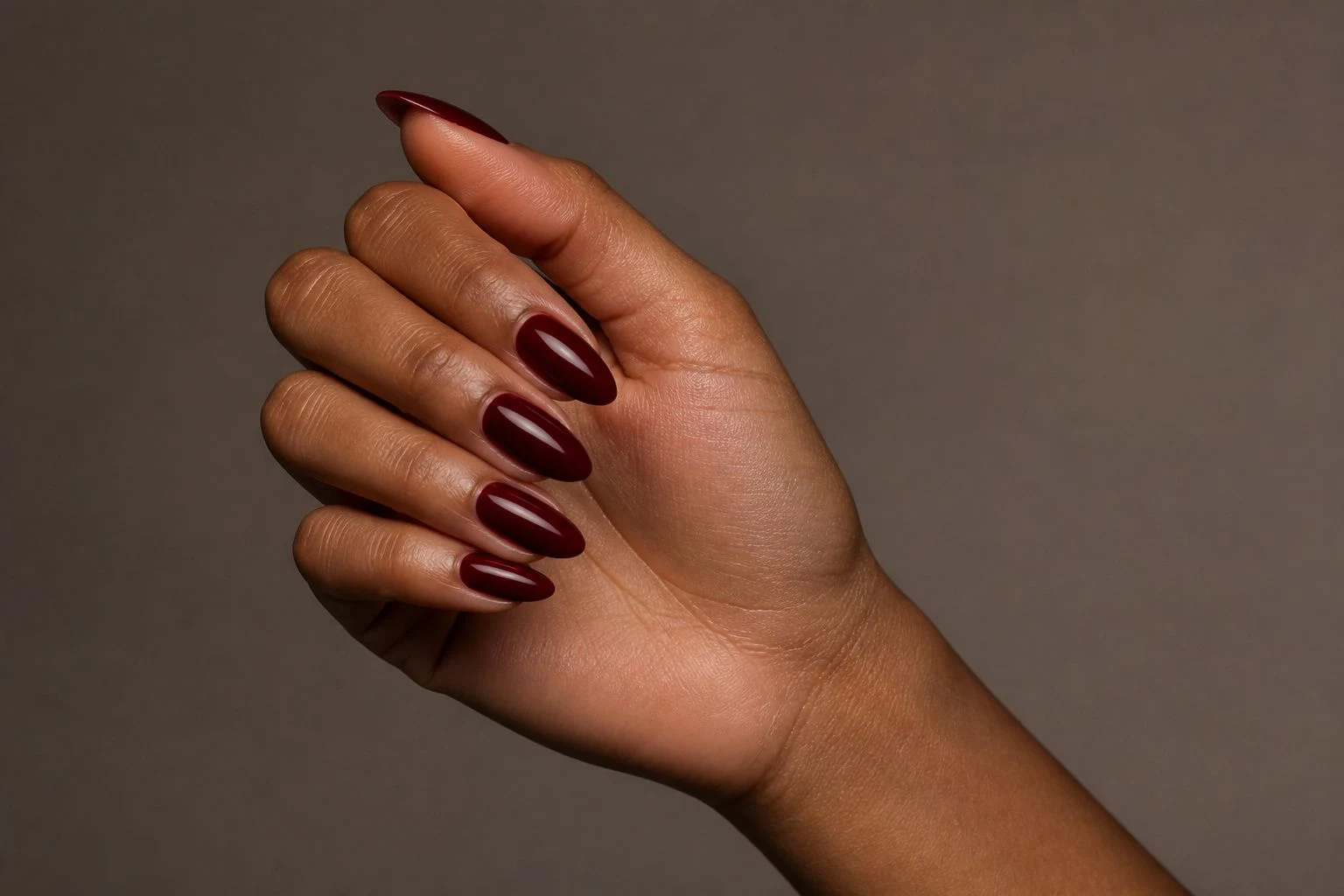 Deep burgundy almond nails in a relaxed curled hand pose showing all five fingers