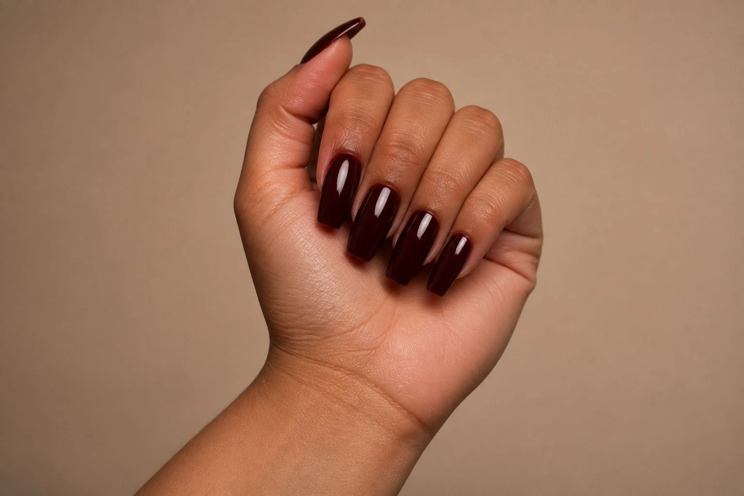 Burgundy coffin shaped nails in a tilted curled hand pose