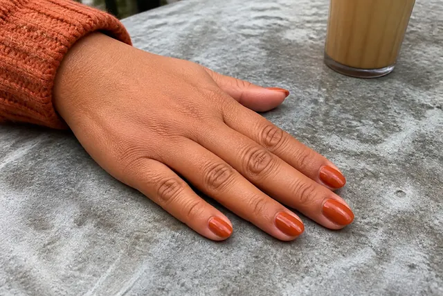 Burnt orange fall nails on a woman’s complete hand in a natural everyday setting.