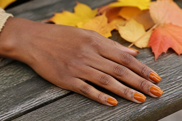 Rust fall nails on a woman’s complete hand in a natural everyday setting.