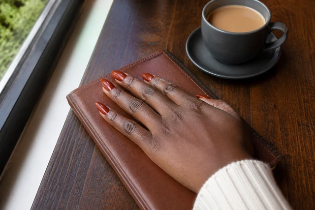 Burnt orange almond fall nails on a woman’s complete hand in a natural everyday setting.