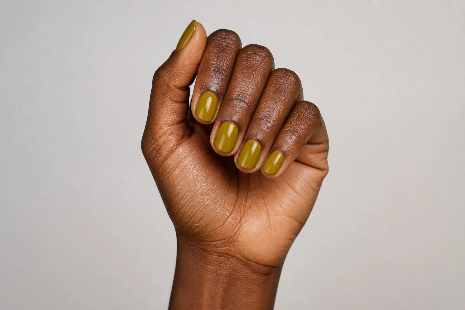 Mustard yellow round nails in a curled hand pose showing all five fingers
