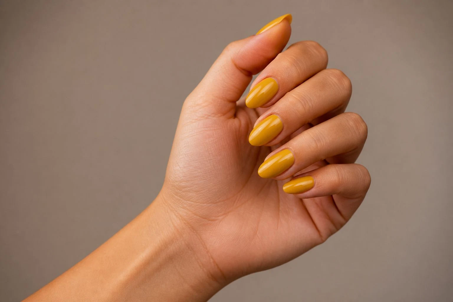 Mustard yellow almond shaped nails in a curled hand pose with wrist turned outward