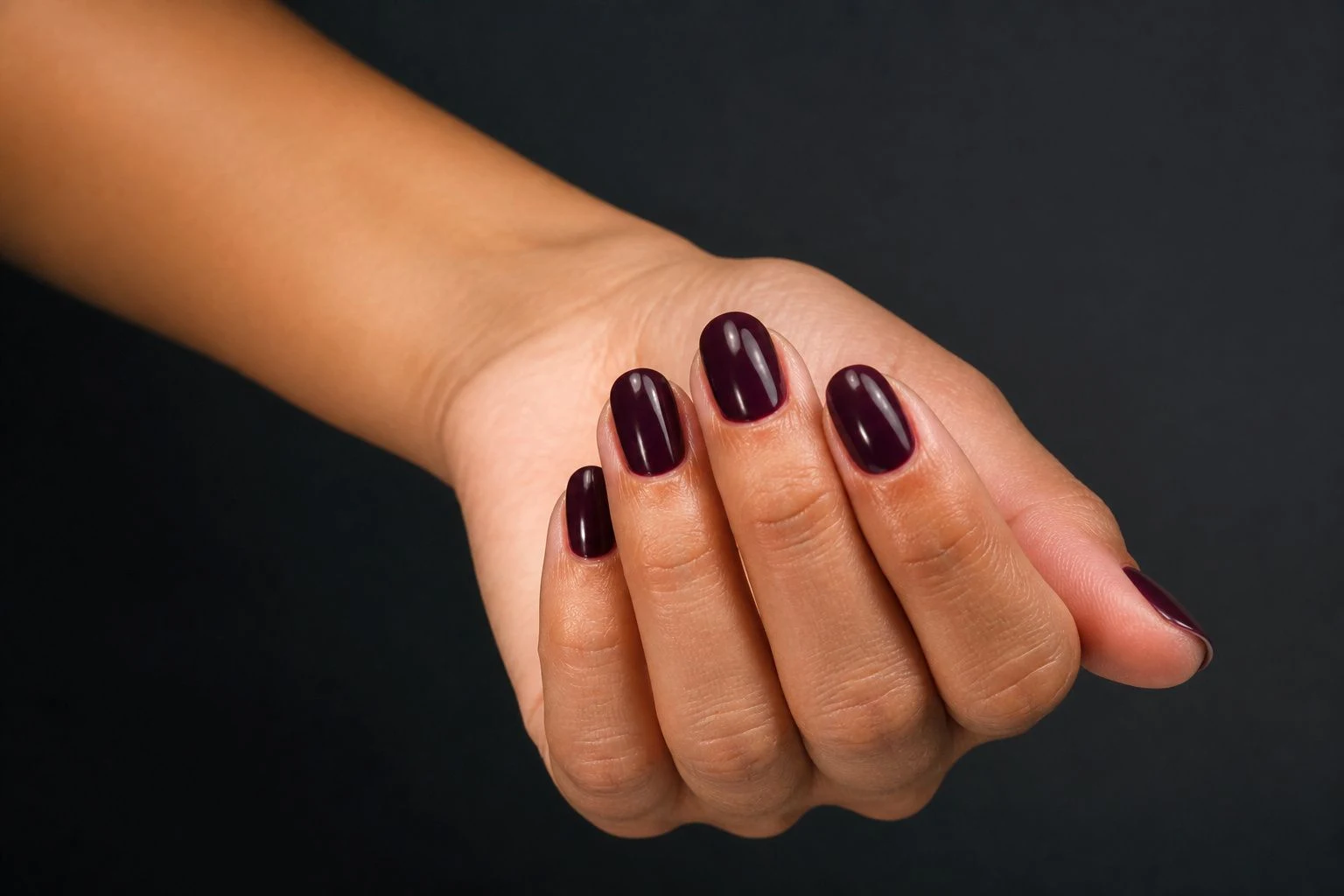 Deep plum round nails in a relaxed curled hand pose