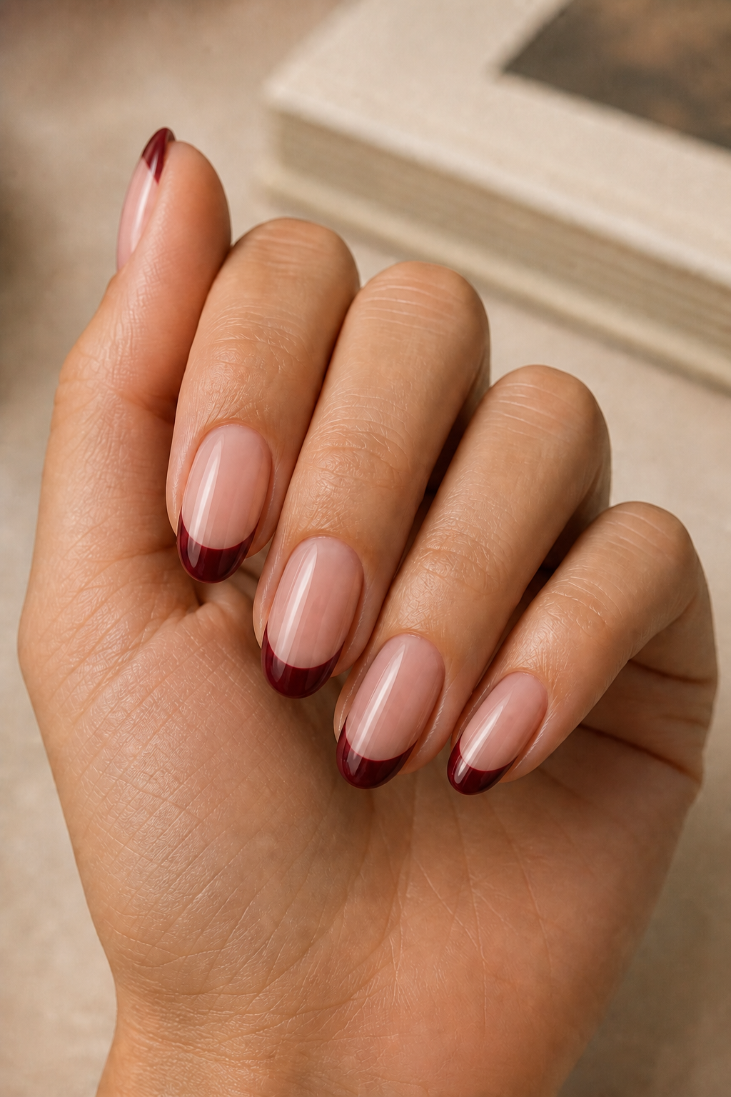 Burgundy French tip fall nails on a woman’s hand with gold rings.