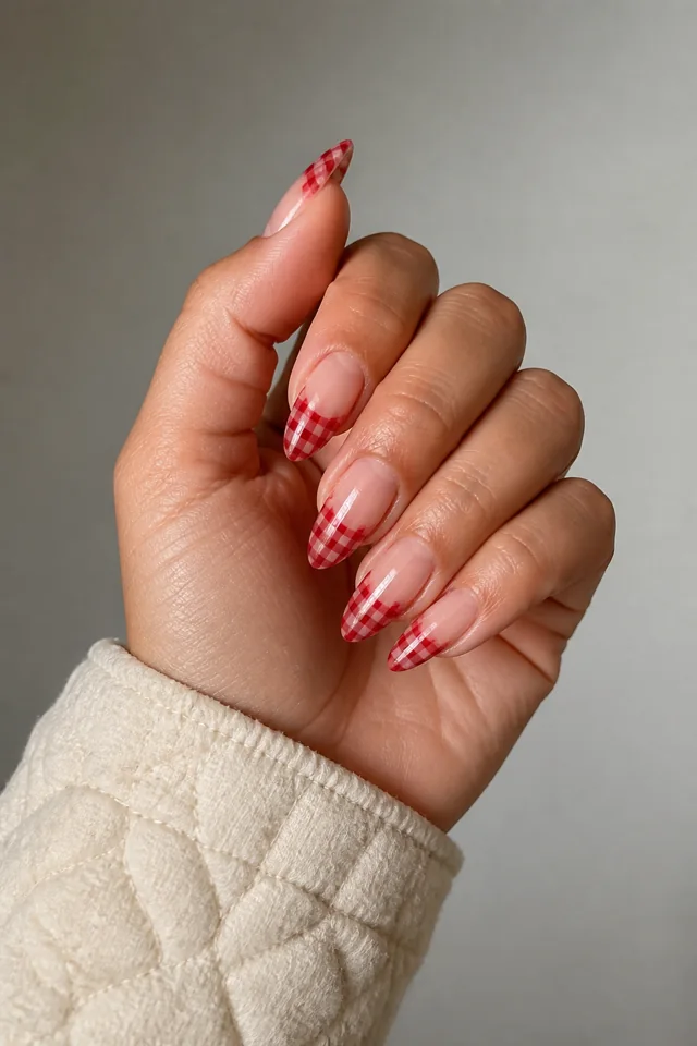 Cherry red gingham across a sheer almond tip, glossy finish, medium skin, hand raised in soft daylight with a connected forearm
