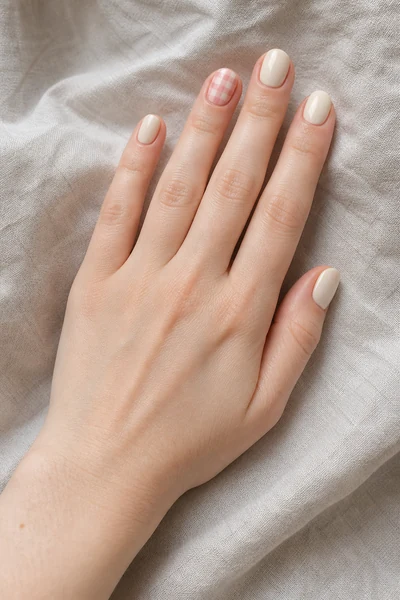Pink and cream gingham accent on short oval nails with glossy finish, relaxed diagonal hand pose, fair skin tone