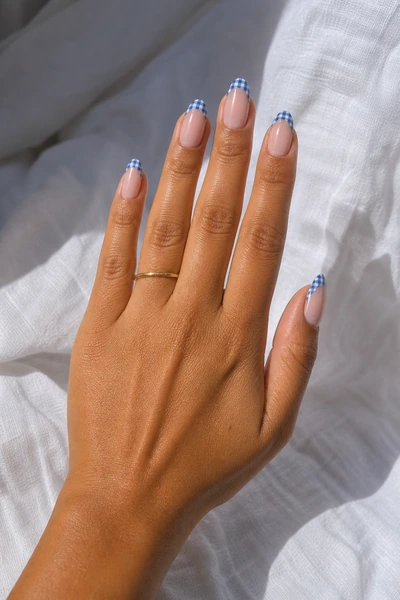 Blue and white gingham French tips on medium almond nails with glossy finish, fingers angled forward, light skin tone