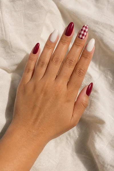 Cranberry and cream gingham accent on medium almond nails with glossy finish, relaxed hand pose, tan skin tone