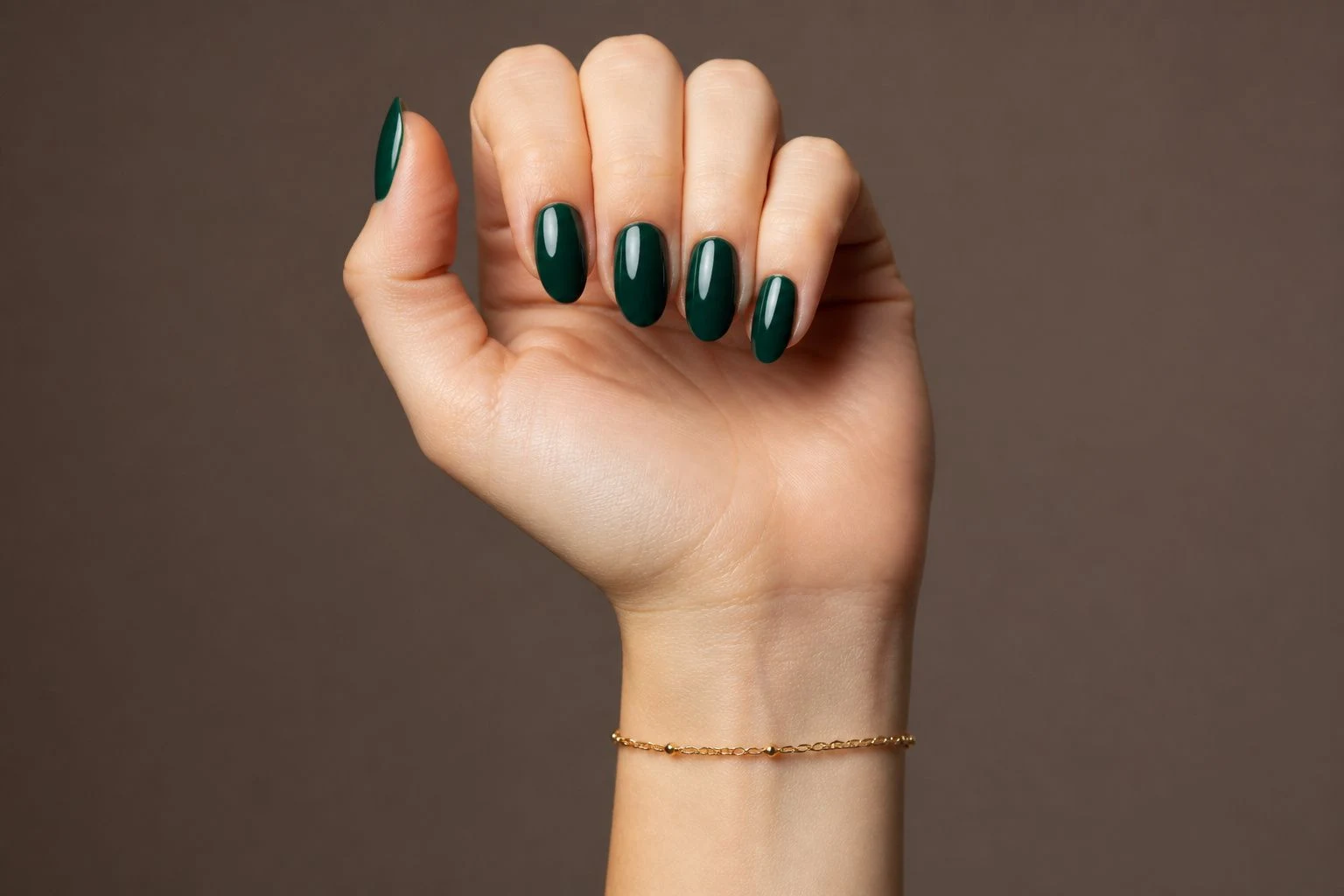 Deep emerald almond Christmas nails in a curled hand pose with a delicate gold bracelet