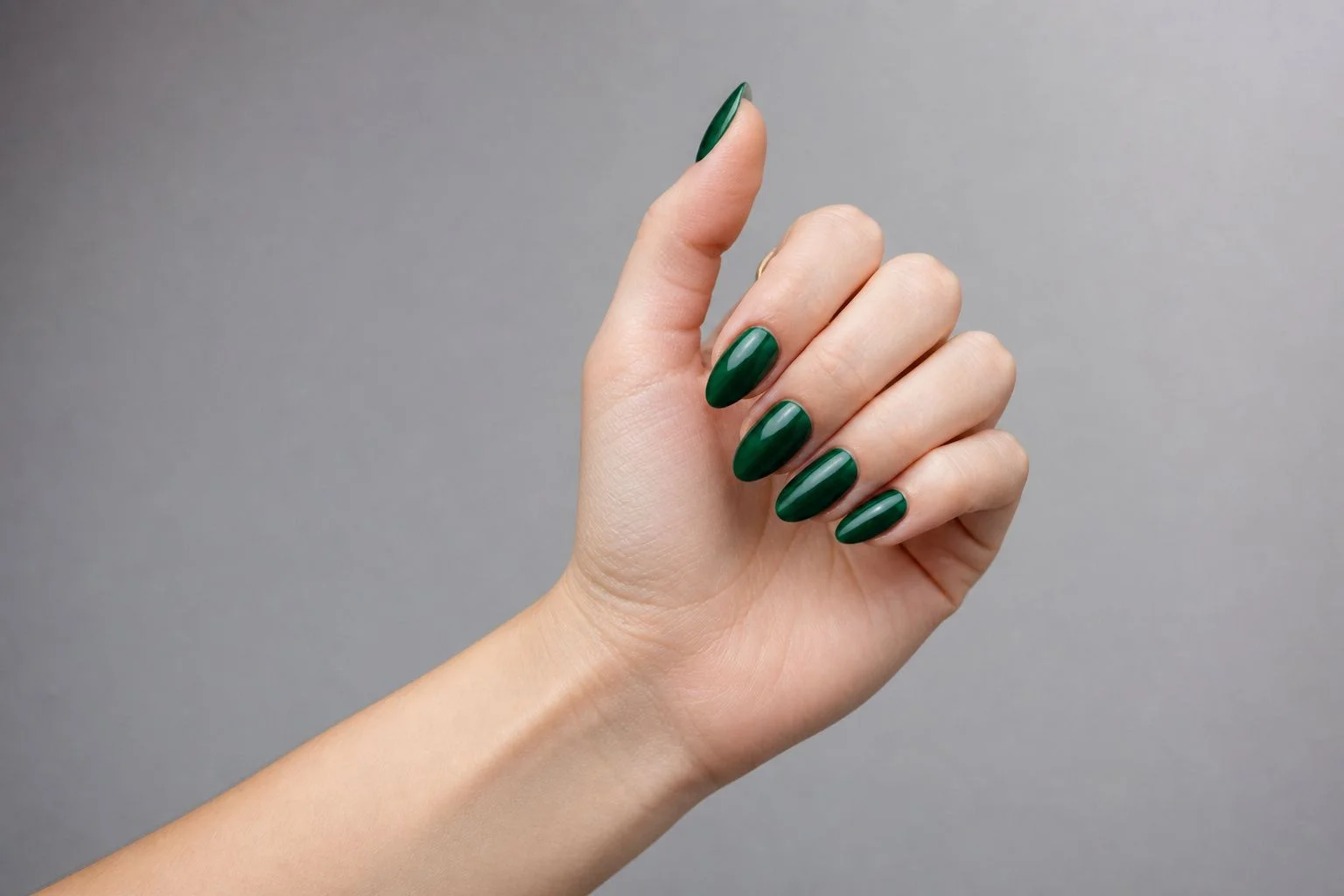 Curled hand with fingers peeking showing a glossy deep emerald green almond manicure and a delicate gold ring