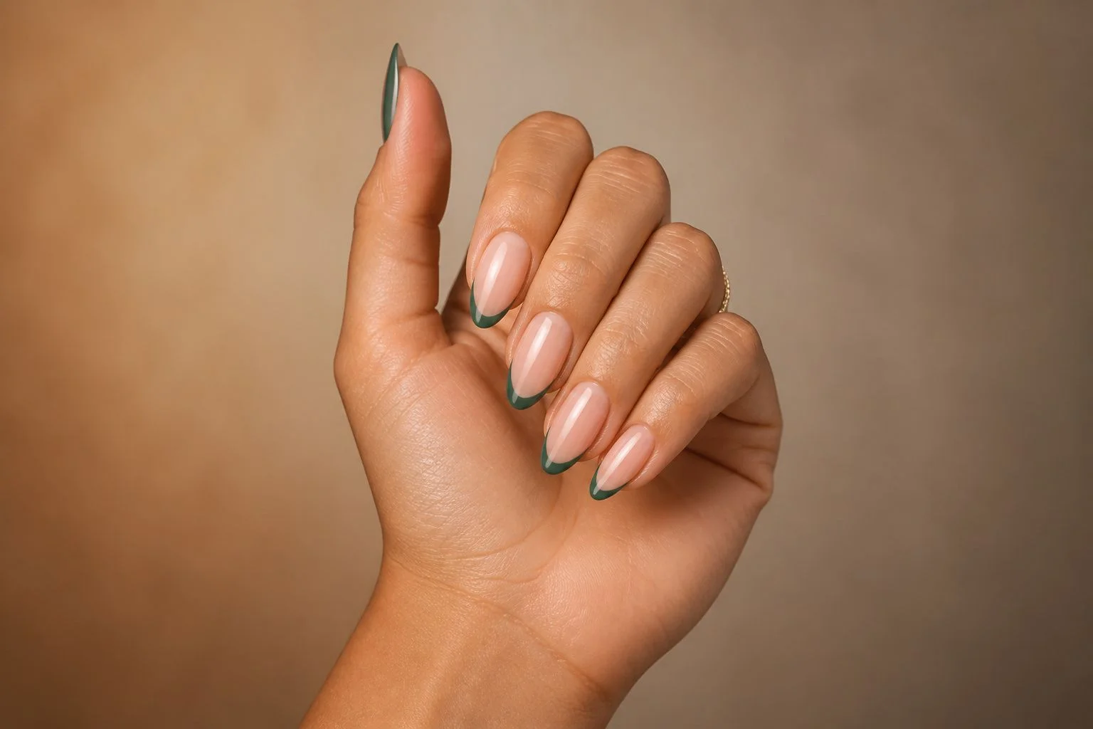 Softly clasped curled hand showing a glossy nude almond manicure with a classic green French tip accent and a delicate gold ring