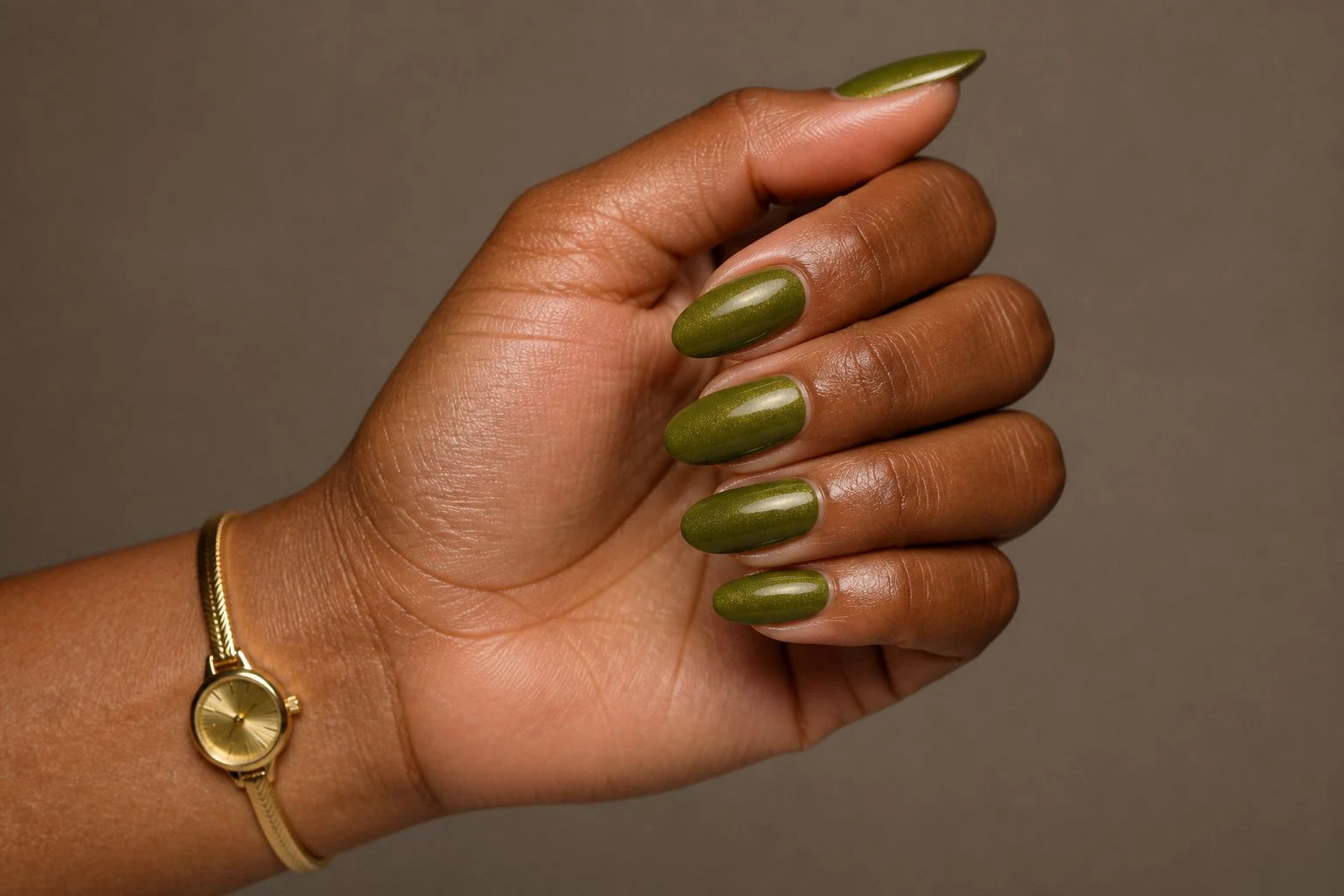 Olive green almond nails with a subtle shimmer in a curled hand pose with a delicate gold watch