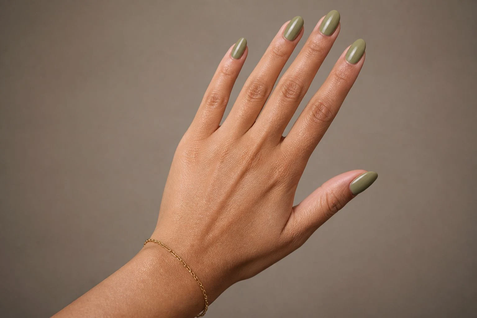 Soft sage almond Christmas nails with a delicate gold bracelet, back of hand pose