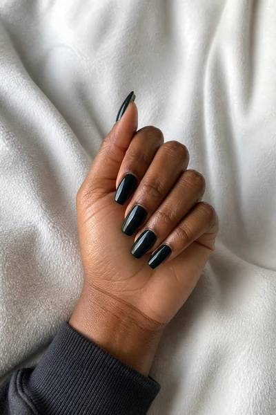 Near-black evergreen coffin nails on a deep brown skin tone hand in a fingertip-rest pose with visible wrist and short partial forearm, natural daylight