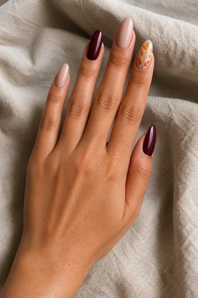Burgundy and golden harvest leaf manicure on medium almond nails with glossy finish, lifted hand pose, tan skin tone