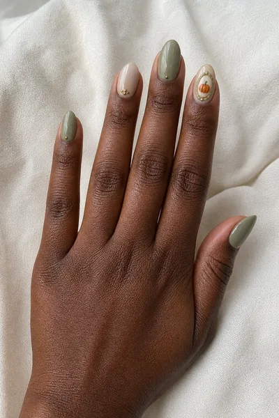 Sage framed harvest pumpkin accent on medium almond nails with glossy finish, lifted wrist pose, deep brown skin tone