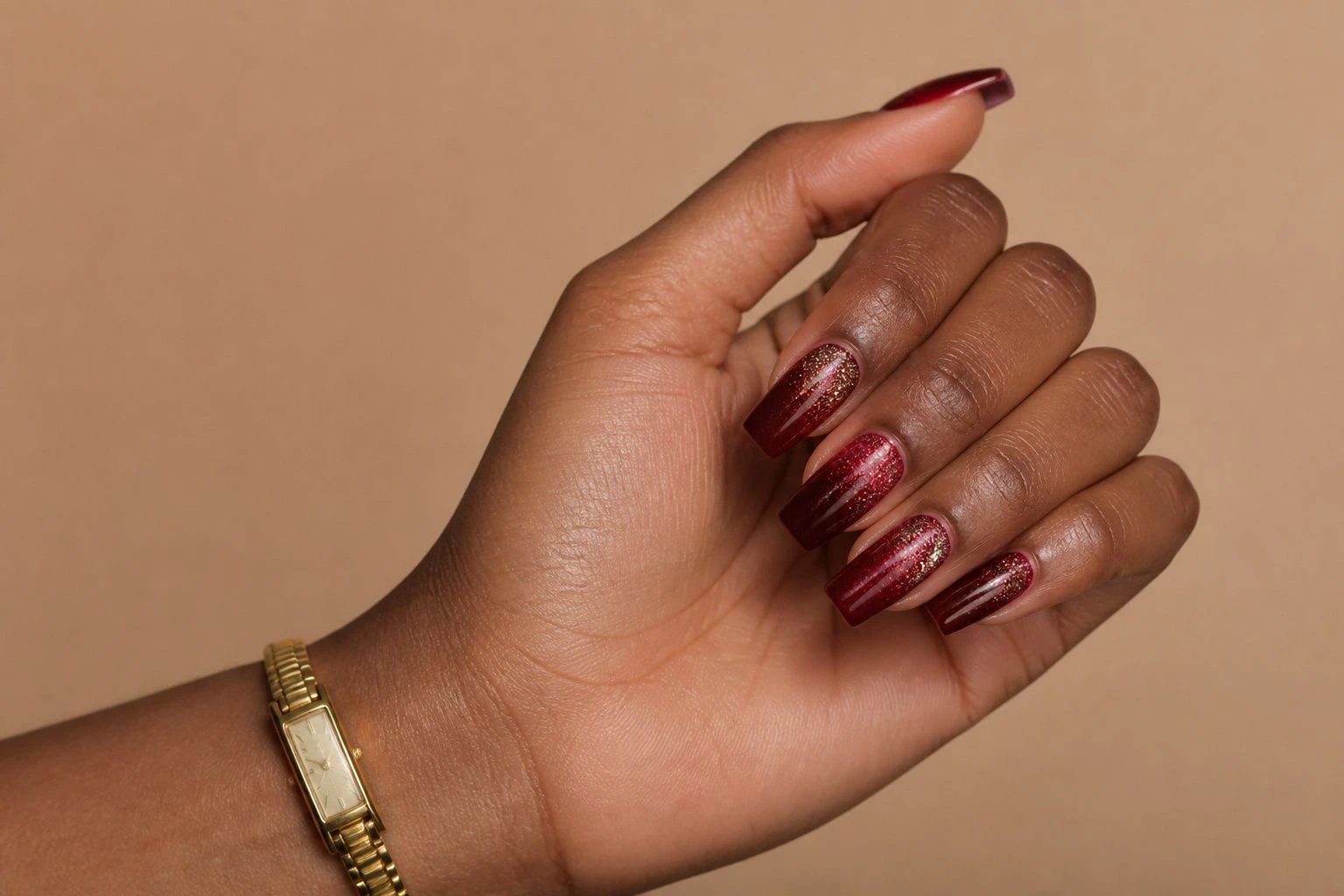 Long coffin shaped garnet red nails with a glitter fade and a slim gold watch, Christmas nail idea