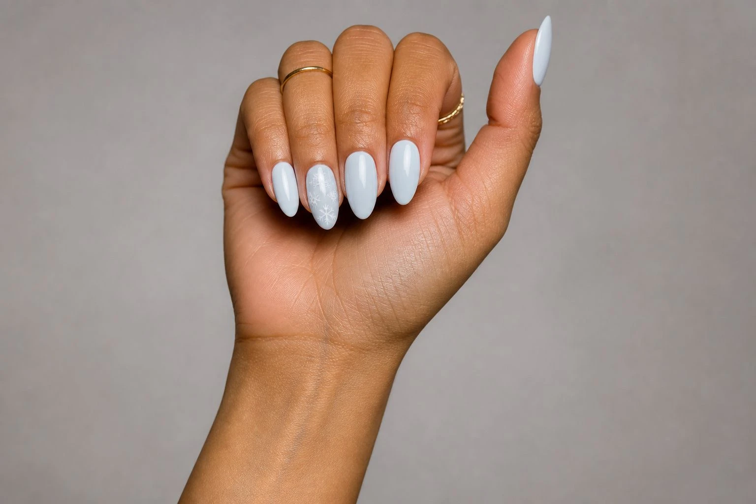 Pale blue white almond nails with a cluster of three snowflakes on the accent nail and two gold rings, Christmas nail idea