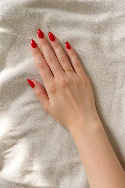 glossy classic red acrylic almond nails on a light warm hand with visible wrist