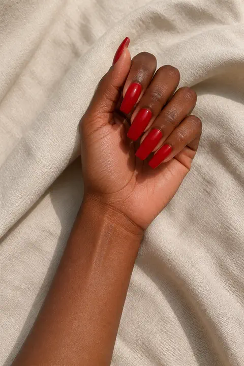 long coffin shaped glossy red acrylic nails on a medium skin tone hand with visible wrist