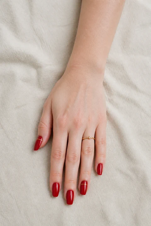 red acrylic nails with delicate rose gold foil on a tan skin tone hand with visible wrist and forearm