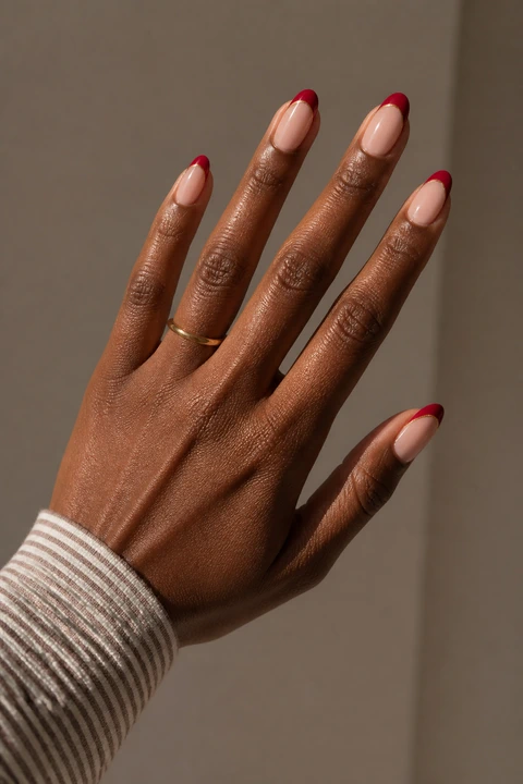 ruby red French tips with a fine gold outline on a medium brown hand with visible wrist