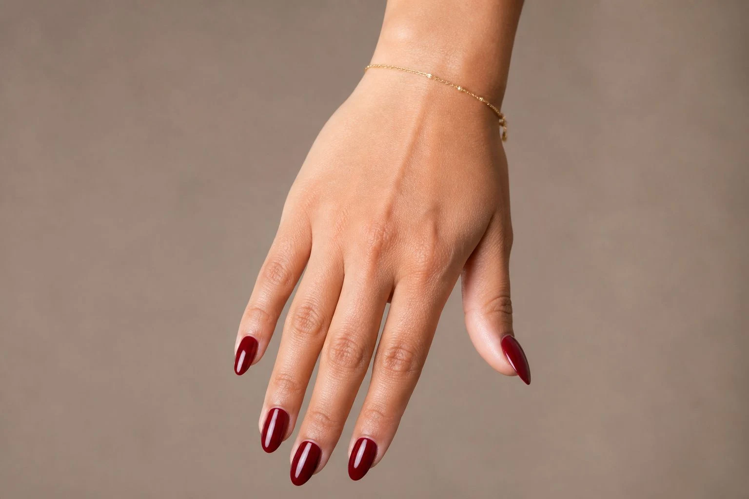 Deep Wine Gel Almond Christmas nails with a delicate gold bracelet