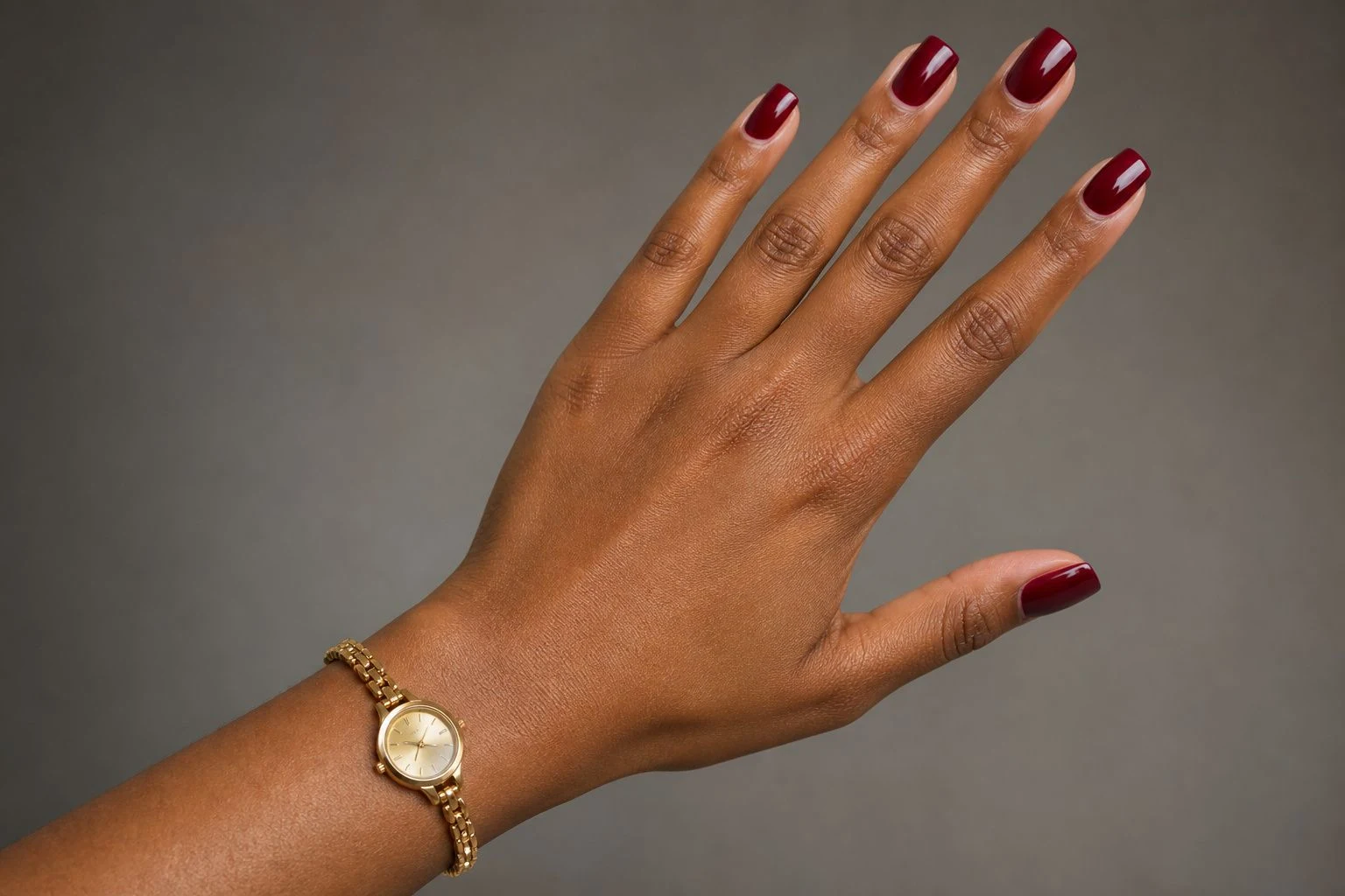 Merlot square Christmas nails in a diagonal hand pose with a delicate gold watch